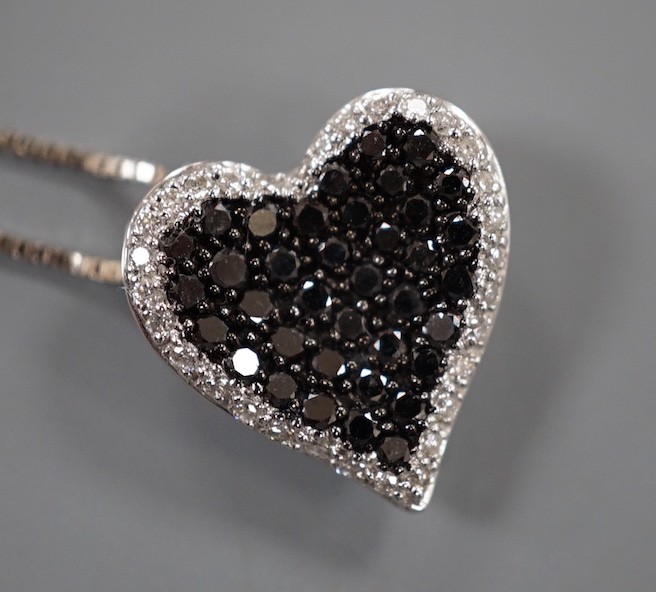 A modern 18ct white gold and pave set white and black diamond set heart shaped pendant, 16mm, on an 18ct white gold fine link chain, 45cm, gross weight 4.4 grams